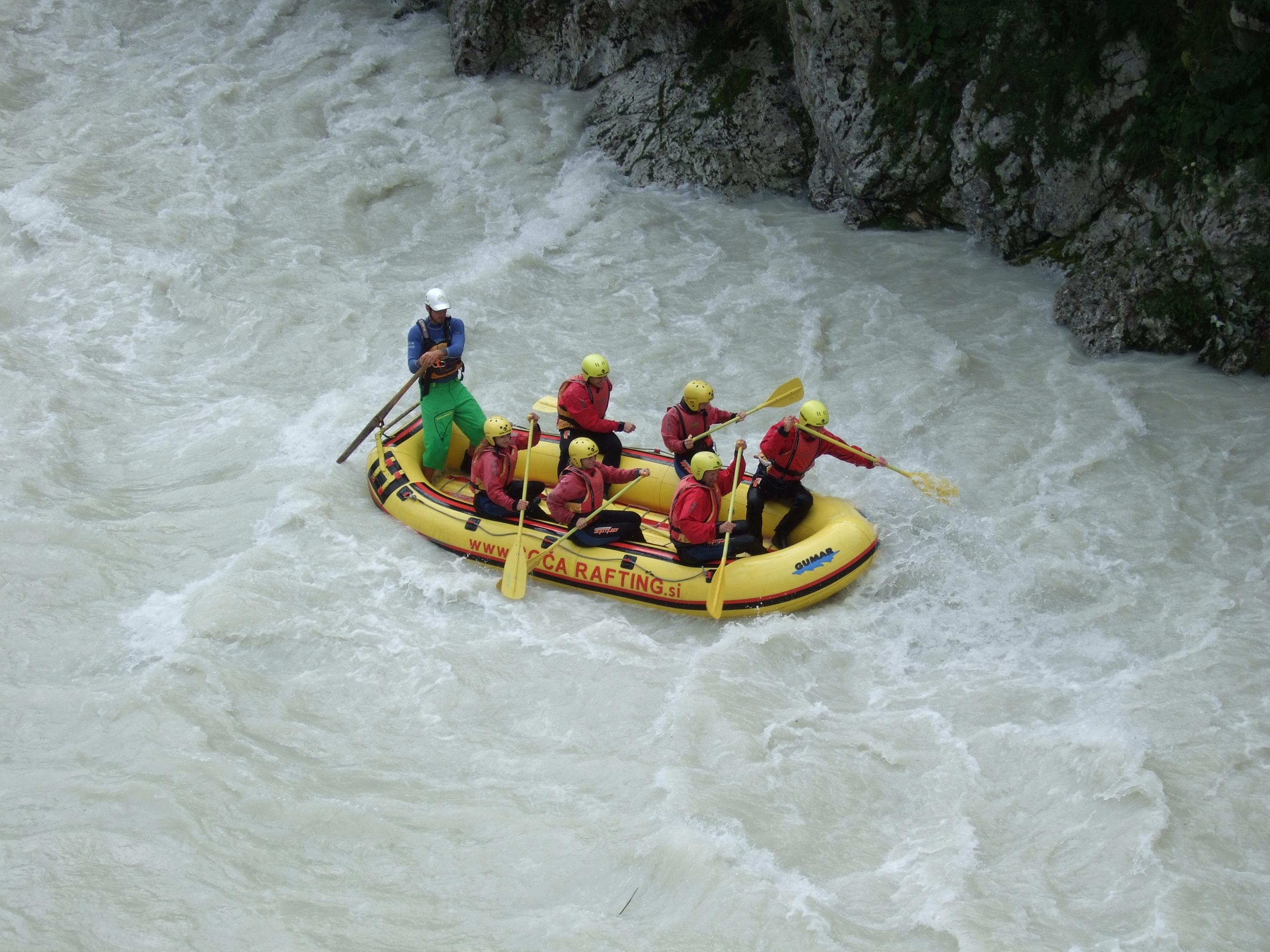 A guide and helmeted paddlers rafting whitewater on the Soča River near Bovec